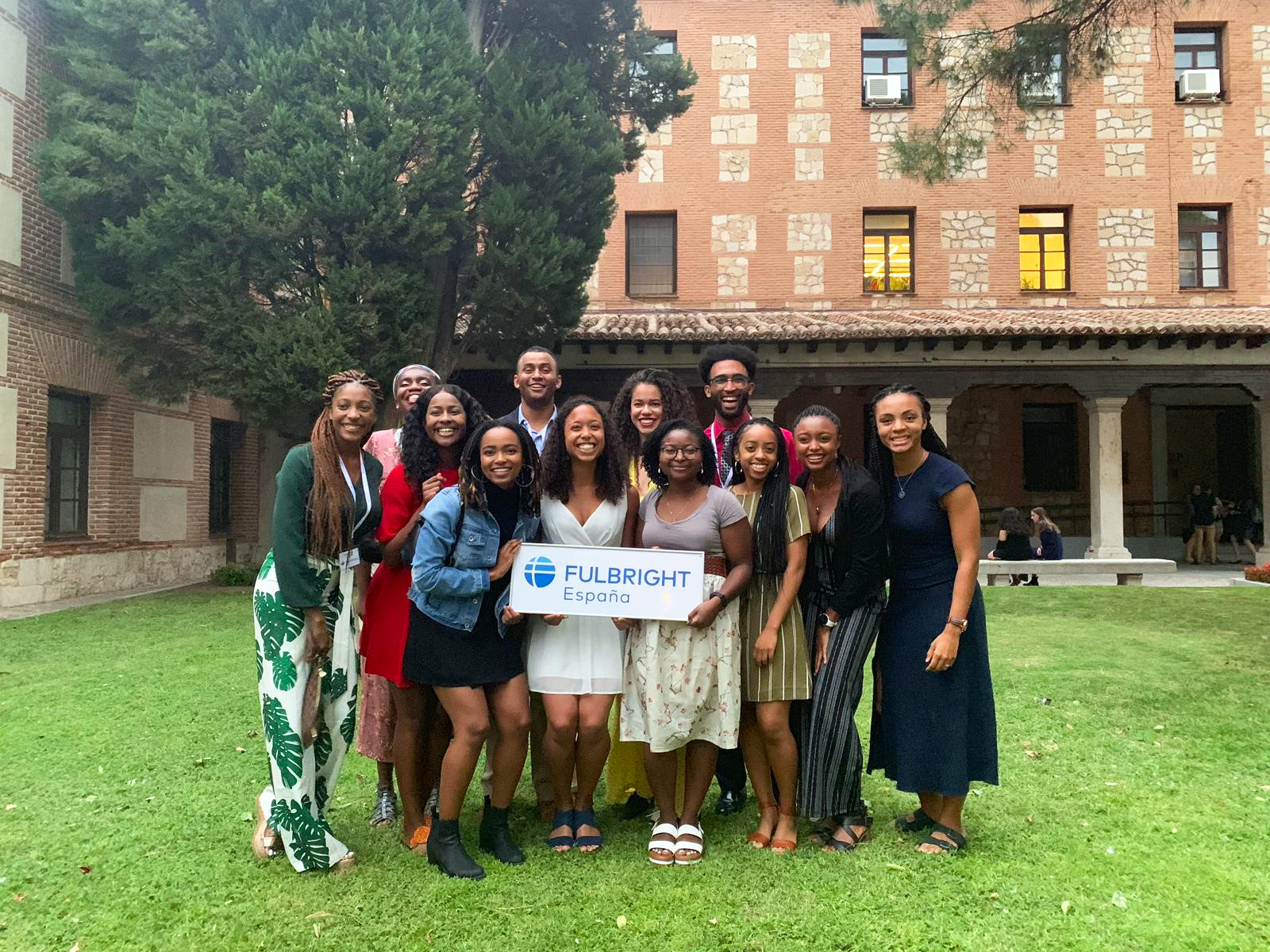 A group of newly appointed Fulbright grantees gather in a huddle, smiling at the camera. Some of the grantees in the middle hold up a sign reading FULBRIGHT ESPANIA. This group from 2019 is all Black students and professionals.